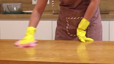Odayı temizliyorum. Önlük giymiş tanınmayan bir kadın ve eldivenler masanın tozunu ve pisliğini temizler. Sarı eldivenli eller yakın plan. Kadın, masayı yapışkan bir bezle siler. Temizlik servisi