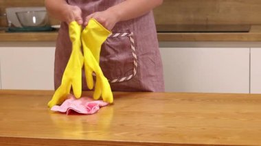 Odayı temizliyorum. Önlük giymiş tanınmayan bir kadın ve eldivenler masanın tozunu ve pisliğini temizler. Sarı eldivenli eller yakın plan. Kadın, masayı yapışkan bir bezle siler. Temizlik servisi