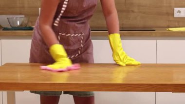 Odayı temizliyorum. Önlük giymiş tanınmayan bir kadın ve eldivenler masanın tozunu ve pisliğini temizler. Sarı eldivenli eller yakın plan. Kadın, masayı yapışkan bir bezle siler. Temizlik servisi