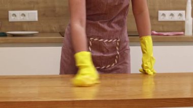 Odayı temizliyorum. Önlük giymiş tanınmayan bir kadın ve eldivenler masanın tozunu ve pisliğini temizler. Sarı eldivenli eller yakın plan. Kadın, masayı yapışkan bir bezle siler. Temizlik servisi