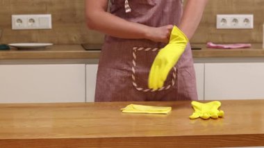 Odayı temizliyorum. Önlük giymiş tanınmayan bir kadın ve eldivenler masanın tozunu ve pisliğini temizler. Sarı eldivenli eller yakın plan. Kadın, masayı yapışkan bir bezle siler. Temizlik servisi