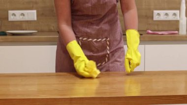 Odayı temizliyorum. Önlük giymiş tanınmayan bir kadın ve eldivenler masanın tozunu ve pisliğini temizler. Sarı eldivenli eller yakın plan. Kadın, masayı yapışkan bir bezle siler. Temizlik servisi