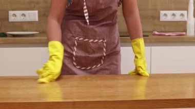 Odayı temizliyorum. Önlük giymiş tanınmayan bir kadın ve eldivenler masanın tozunu ve pisliğini temizler. Sarı eldivenli eller yakın plan. Kadın, masayı yapışkan bir bezle siler. Temizlik servisi