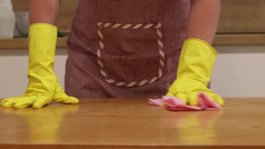 Odayı temizliyorum. Önlük giymiş tanınmayan bir kadın ve eldivenler masanın tozunu ve pisliğini temizler. Sarı eldivenli eller yakın plan. Kadın, masayı yapışkan bir bezle siler. Temizlik servisi