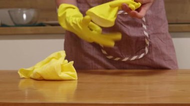 Odayı temizliyorum. Önlük giymiş tanınmayan bir kadın ve eldivenler masanın tozunu ve pisliğini temizler. Sarı eldivenli eller yakın plan. Kadın, masayı yapışkan bir bezle siler. Temizlik servisi