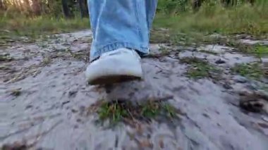 Beyaz spor ayakkabılarla ormanın zemininden yürüyen kadın bacakları. Doğada yaz yürüyüşü. Parkta yürüyen biri. Ön manzara. Akşam yürüyüşü