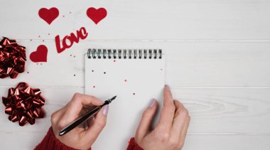 Kadının elleri not defterine Sevgililer Günü 'nü romantik bir şekilde kutluyor. Sevgililer Günü tatili konsepti. Üst Manzara. Boşluğu kopyala.
