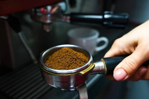 The barista\'s hand holds a holder with ground fresh coffee for making coffee in a coffee machine. Close-up. Selective focus.