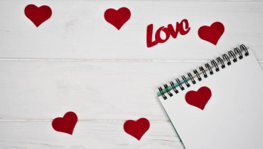Sevgililer Günü 'ne romantik tebrikler. Kırmızı kalpler, not defteri ve beyaz ahşap arka planda aşk kelimesi. Üst Manzara. Mesaj için yer. Pankart.