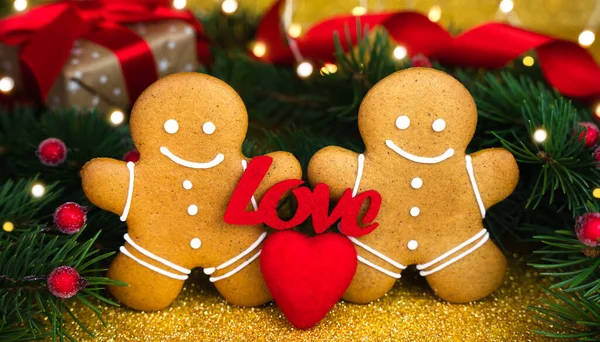 Two gingerbread men, the word LOVE and red heart on glitter golden background. Concept for Valentine\'s day. Close-up.