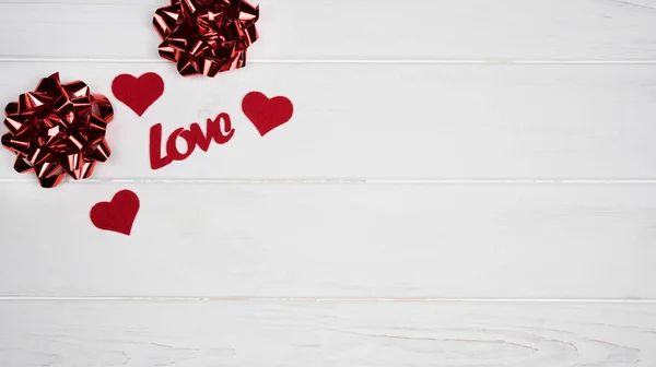 Festive decor for Valentine\'s Day with red hearts, bows and word Love on white background. Banner. Top view. Flatlay. Copy space.