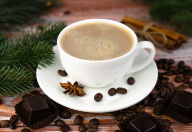 Bir fincan sıcak kapuçino, çikolatalı şekerler ve ahşap arka planda dağınık kahve çekirdekleri. Yakın plan. Seçici odak.