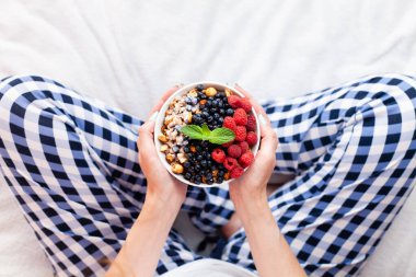 Womans hands hold a bowl of granola with fresh with fresh berries. Healthy breakfast in the morning. Top view. Selective focus.