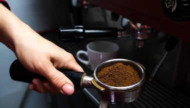 The barista's hand holds a holder with ground fresh coffee. Making coffee in a coffee machine in cafe. Close-up. Selective focus.