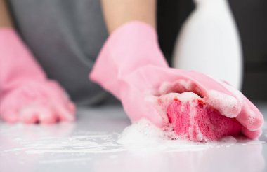 A girl in rubber gloves washes the table with detergent. Concept of spring cleaning. Close-up. Selective focus.