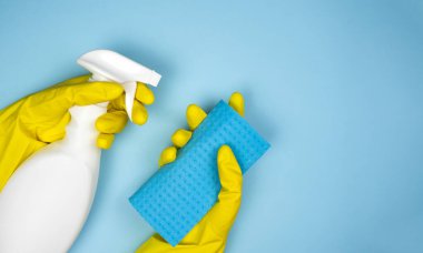 Woman's hands in rubber gloves hold a cleaner and rag on a blue background. Housekeeping concept. Close-up. Copy space. Top view.