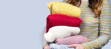 Genç bir kız elinde çok renkli örülmüş kalın kazaklar tutuyor. Sonbahar ve kış giysileri. Pankart. Uzayı kopyala Seçici odak.