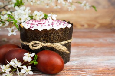 Renkli kırmızı yumurtalar, Paskalya pastası ve ahşap masada çiçek açan kiraz dalları. Yakın plan. Mesaj için yer. Seçici odak.