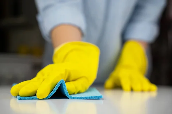 Housewife in yellow rubber gloves wipes the kitchen table with a rag. Housekeeping concept. Close-up. Selective focus.