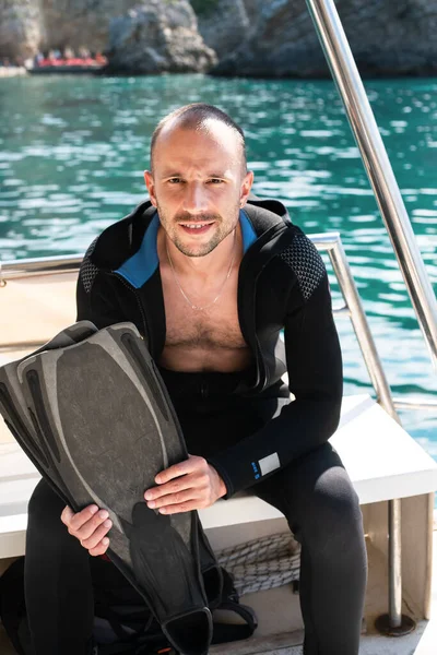 Genç bir dalış dalgıcı teknede yüzgeçlerini tutuyor. Dalış dersleri. Denizde dinleniyor. Seçici odak.