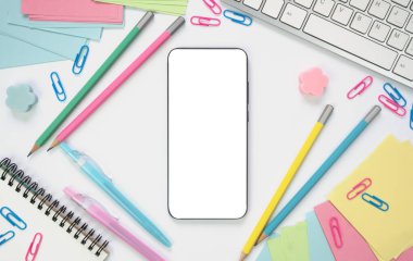 Masada beyaz ekranlı akıllı telefon ve okul malzemeleri var. Çevrimiçi öğrenme kavramı. Modelleme. Flatlay. Üst Manzara. Boşluğu kopyala.