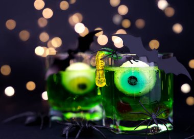 Festive Halloween party. Green cocktails with eyes and jelly worms in a glass and spiders and bats on a black background. Close-up. Selective focus. clipart