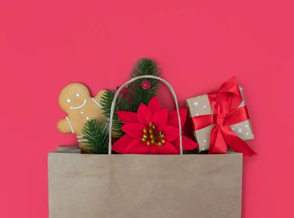 Christmas gifts in paper eco bag on on a red background. Festive flatlay composition. Holiday gift shopping concept. Copy space. Top view. Close-up.
