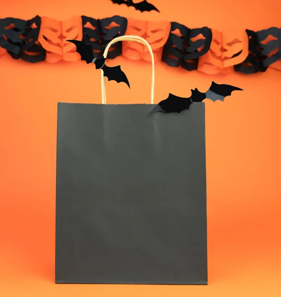 Paper black bag and decor for Halloween on orange background. Halloween shopping concept. Mock up. Copy space. Selective focus.