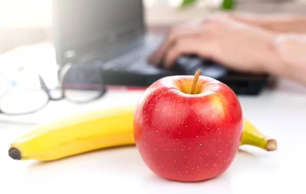 A red apple and banana on the desktop. The concept of a healthy food at work. Close-up. Selective focus.