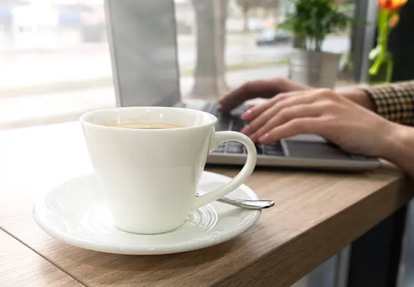 カフェでラップトップで働く女の子のテーブルと手の上のコーヒー オンラインで働く クローズアップ 選択的なフォーカス ロイヤリティフリーのストック写真