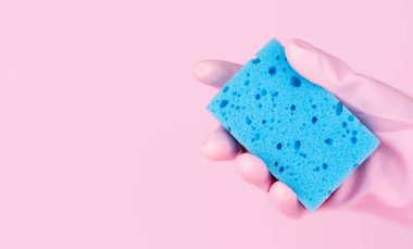 A hand in pink rubber glove holds a cleaning sponge on a pink background. Copy space. Banner. Selective focus.