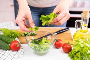 Genç bir kadın cam kaseye marul yaprakları koyar. Sağlıklı ve beslenme salatası hazırlığı. Sağlıklı Yaşam Tarzı.