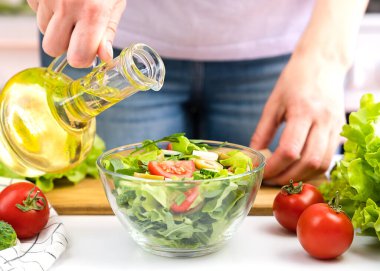 Kadının elleri sebze salatasına zeytinyağı döküyor. Yakın plan. Seçici odak.