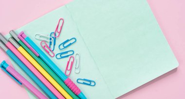 Renkli kalemler, kalemler ve pembe bir not defteri. Okula dönelim. Mesaj için yer var. Flatlay. Üst görünüm.