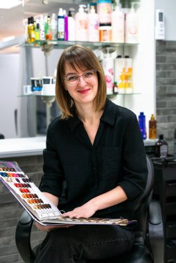 Gülen kız kuaför elinde paletle saç boyası örnekleri tutuyor. Boyama, saç rengini değiştirme, güvenli saç bakım konsepti. Seçici odak.