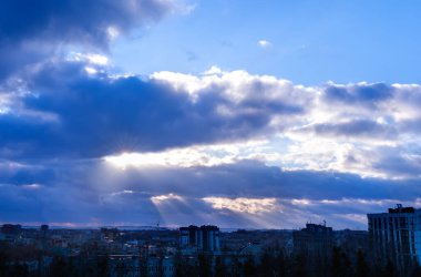 Çarpıcı koyu mavi gökyüzü ve bulutların arasından şehrin arka planına vuran güneş ışınları. Seçici odak.
