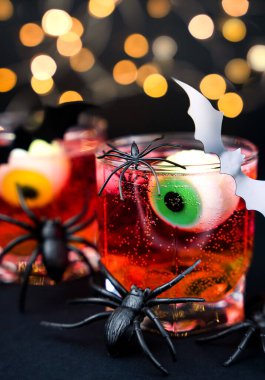 Cadılar Bayramı partisinde ürkütücü süslemelerle kırmızı kokteyl, şekerli gözler, örümcekler ve yarasa, Cadılar Bayramı kutlaması için bayram içeceği. Yakın plan. Seçici odak.