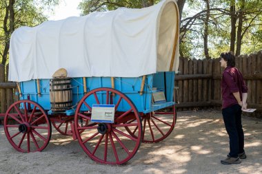 Cenova, NV, ABD. 2022-09-17. Mormon İstasyonu Tarih Parkı 'nda kırmızı tekerlekleri olan mavi çayır öğrenci vagonuna bakan kimliği belirsiz genç adam.. 