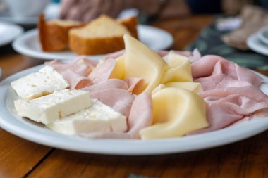 Brazilian breakfast concept with Minas cheese (queijo minas), ham and Prato cheese (queijo Prato) served with corn bread, under natural light, realistic photo taken in a real establishment