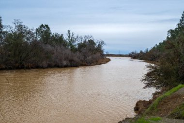 Putah Creek in Winters, California, USA , on a partly cloudy day after heavy rains, brown color of water and sky copy-spac