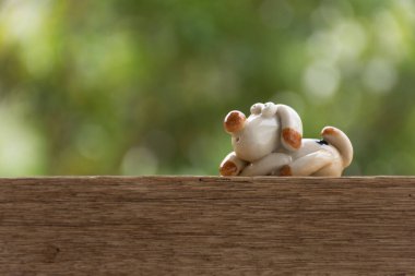 Bu seramik bebek oturup bir şey düşünüyor. Ahşap arka planda yapraklar yeşile bokeh.