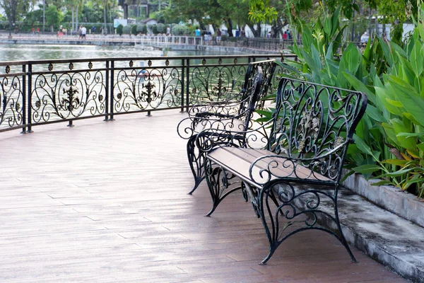 stock image At a shady public park on a wooden terrace by the river, there are two bench waiting for people to sit. Bench made of wrought iron with beautiful designs.