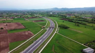 Hava aracı görüntüsü. Tarımsal tarlalar ve yeşil kırsal alanların arasından geçen beyaz araba, takip eden araçlar. Yüksek kalite 4k görüntü