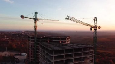 İHA bakış açısı inşaat alanındaki gün batımında vinç kulesinin etrafında hareket ediyor. İnşaat alanındaki vinç kulesinin kaldırma malzemesinin görüntüsünü kapat. Sanayi inşaat konsepti Şangay Çin görüntüsü