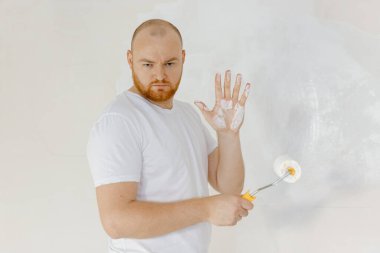 Beyaz duvarı boyarken ve tadilat yaparken 30 'lu yaşlarda gülümseyen bir adamın portresi.