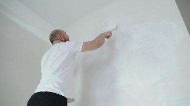 Dairenin tamiri - profesyonel boyacı duvarları beyaz boya silindiriyle boyuyor. Yüksek kalite 4k görüntü