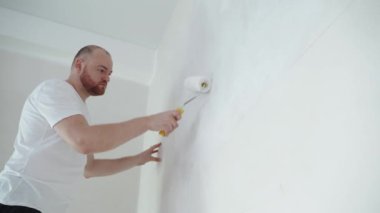Bir adam silindirle duvar boyuyor. Odada tamirat yapan bir adam. Modern iç mekan. Yüksek kaliteli onarım