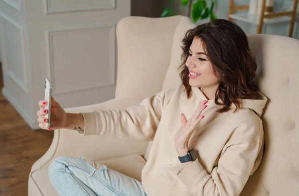 Closeup image of a beautiful woman waving hands while using mobile phone for video call at home. High quality photo