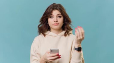 A brunette teenage girl has a perplexed expression as she holds her smartphone and trying to find an answer to the problem in front of her. Her gesture of having no idea and shrugging her shoulders