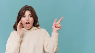 This teenage girls smiling face and pointing gesture towards the copy space in the background creates a playful and happy atmosphere in this studio shot, perfectly capturing the carefree spirit of